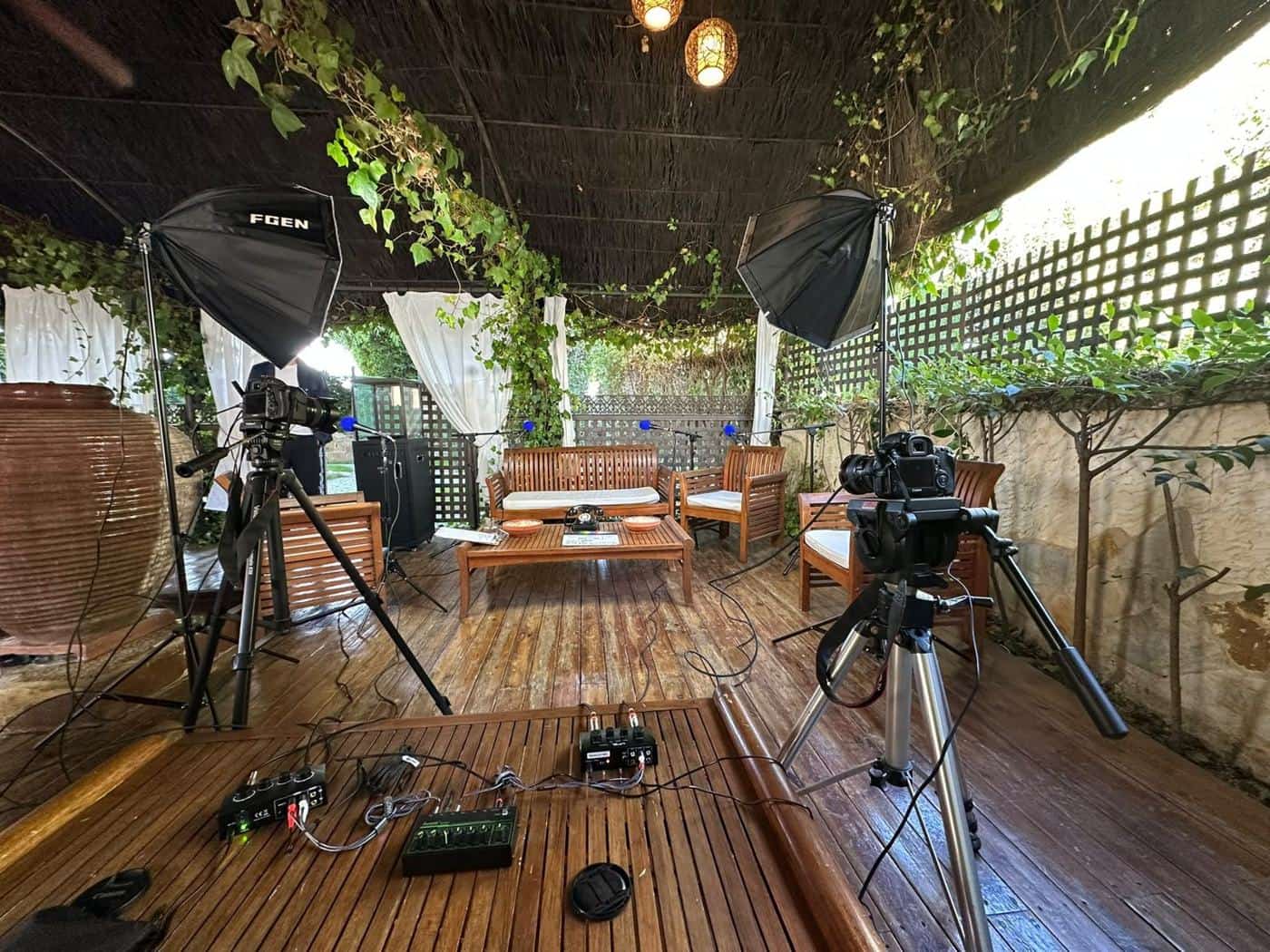 Set de grabación de Podcast Boda bajo una pérgola: sofá de madera, dos cámaras, focos y micrófonos